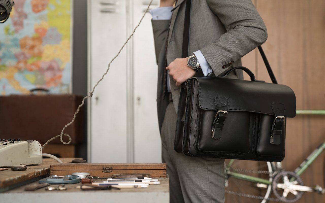 Man carrying his black leather satchel briefcase with asymmetric front pockets on the shoulder.
