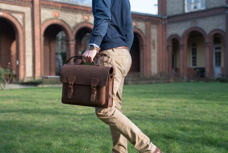 Elegant man holding the brown leather satchel by the handle.